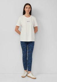 T-shirt en coton blanc à manches courtes avec texte imprimé. Leggings à motif zèbre bleu et noir. Baskets blanches avec des accents beiges.