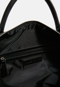 Black nylon handbag interior with smooth texture, featuring a zippered pocket and a branded leather label. Silver hardware along the opening.
