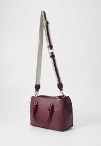 Burgundy handbag with a structured design, textured leather, two top handles, and a detachable strap featuring grey and maroon accents.