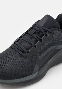 Chaussure de sport noire avec tige en mesh, fermeture à lacets, accents texturés et semelle en caoutchouc. Présente un logo subtil sur le côté et du rembourrage.