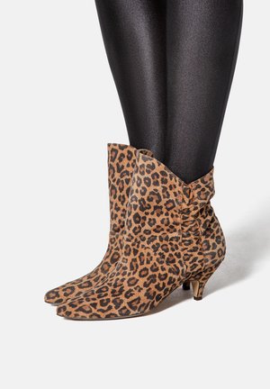 Stivali alla caviglia con stampa leopardata, punta affusolata, texture morbida, tacco di altezza media e dettagli arricciati nella parte superiore. Leggings neri sotto.