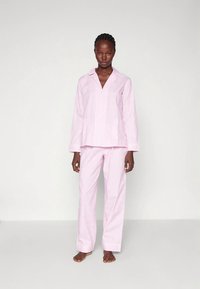 Rdeč roza bombažni pižama komplet s srajco z ovratnikom in gumbi ter dolgimi rokavi ter ohlapnimi hlačami, ki se ujemajo. Gladek tekstura, brez vidnih vzorcev.