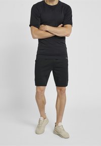 Czarna koszulka sportowa z krótkim rękawem o strukturalnym wykończeniu, w zestawie z czarnymi szortami. Sneakersy w jasnym beżowym odcieniu o masywnej konstrukcji.