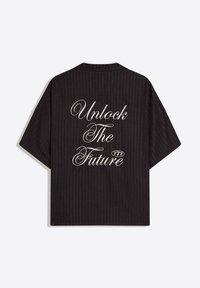 Chemise noire à manches courtes avec fines rayures et texte en écriture blanche au dos indiquant "Unlock The Future 777."