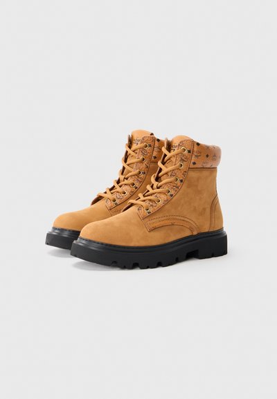 Tan suede boots with a black rubber sole, padded collar, and round toe; features gold eyelets and a patterned trim above the ankle.