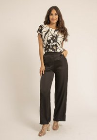 Blouse à motif floral noir et blanc avec une coupe décontractée, associée à un pantalon en satin noir taille haute et des escarpins dorés à lanières.