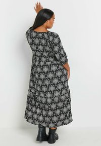 Musta maksimekko valkoisella kukkakuviolla, rento malli, kolmannen osaston hihat ja pyöreä pääntie, käytetty mustien paksupohjaisten saappaiden kanssa.