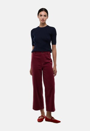 Haut en tricot côtelé marine à manches courtes associé à un pantalon large en velours côtelé bordeaux et des chaussures plates rouges, affichant une coupe décontractée et une texture lisse.