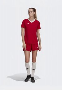 Sarkans futbola krekls un šorti ar baltām detaļām, izgatavoti no sintētiska materiāla. Ceļgalu augstuma baltas zeķes ar melnu logo, kopā ar melnām futbola kurpēm.