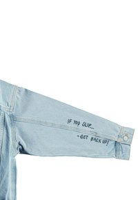 Giubbotto in denim di colore azzurro chiaro, caratterizzato da maniche lunghe con testo stampato: "SE CADI... -RIALZATI!" sull'avambraccio. Dettaglio con bottoni in metallo.