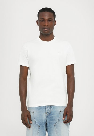 Weißes Baumwoll-T-Shirt mit Rundhalsausschnitt und kurzen Ärmeln, ausgestattet mit einem kleinen Logo auf der linken Brust. Strukturiertes Material, klassischer Schnitt.