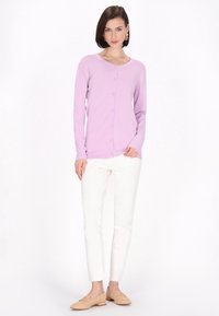 Cardigan lungo viola chiaro con maniche lunghe, scollo rotondo e bottoni frontali, abbinato a pantaloni bianchi slim-fit e mocassini beige.