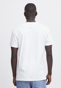 Camiseta de algodón blanca con mangas cortas, cuello redondo y un corte relajado, mostrada desde la parte de atrás frente a un fondo liso.