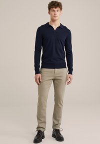 Polo de culoare bleumarin cu mânecă lungă și guler, asortat cu pantaloni bej slim-fit și pantofi negri cu șireturi. Un design simplu, clasic, cu o textură netedă.
