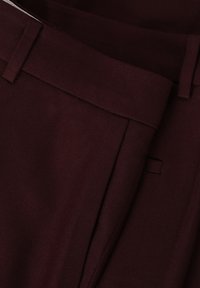 Burgundy op maat gemaakte broeken van gestructureerde stof, met een vlakke voorkant en riemenlussen. Voering in de tailleband met nette stikdetails.
