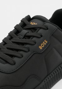 Sneaker sintetico nero con logo "BOSS" dorato a contrasto, dotato di punta rotonda, tessuto testurizzato e lacci neri piatti.