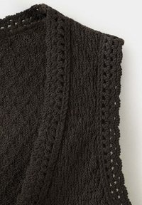 Tissu tricoté au crochet marron foncé avec des motifs texturés et un bord festonné, drapé sur un fond blanc.