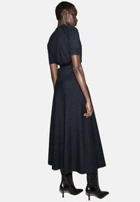 Vestido negro de punto con mangas cortas y cintura ajustada, que fluye hacia una falda amplia. Textura suave; combinado con botas de tacón negras.