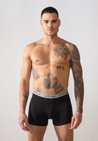 Fekete boxeralsó szürke rugalmas derékpánttal, jellegzetes logóval. Az anyag lágynek tűnik, sima textúrájú és testhezálló kialakítású.