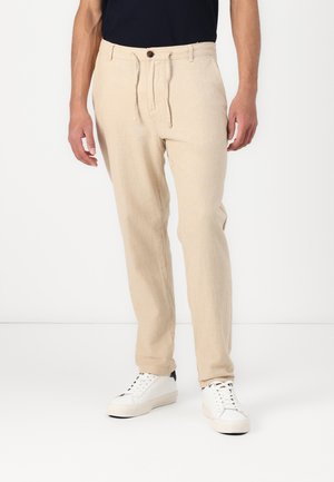 Beige linblandede bukser har en snoreliv, forlommer og en skræddersyet pasform, parret med hvide sneakers.