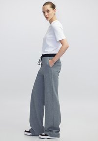 Pantaloni sportivi grigi a gamba larga con vita elastica e cordino, abbinati a una maglietta bianca aderente. Materiale morbido in misto cotone.