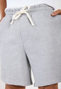 Shorts en coton gris avec une taille élastique et un cordon de serrage ; dotés de poches latérales et d'une texture douce et brossée.