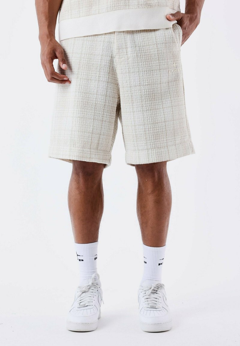Shorts blancs texturés avec un motif à carreaux, dotés d'une coupe droite et de poches latérales, associés à des baskets blanches et des chaussettes.