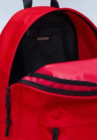 Zaino rosso realizzato in un tessuto liscio e resistente. Presenta un'apertura ampia, un interno nero e una tasca con zip all'interno. Accentuato da accessori neri.