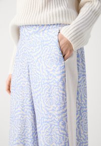 Pantalons larges de couleur bleu clair avec un motif floral en crème. Dispose de poches latérales et d'un panneau en tissu blanc contrastant.