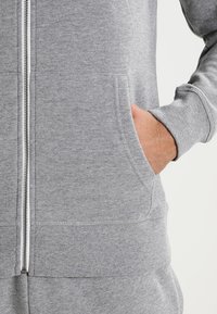 Grå zip-up hoodie i mjuk bomullsblandning. Har framfickor, ribbade ärmslut och en slät yta. Dragkedjan går ner i mitten.