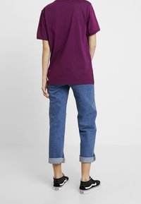 Camiseta corta de algodón morada, de corte holgado, combinada con unos vaqueros de mezclilla azul claro con puños enrollados. Zapatillas negras y blancas completan el conjunto.