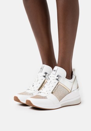 Valkoiset ja metallinhohtoiset tennarit, joissa on teksturoitu kulta- ja hopeakoriste, nauhallinen etuosa sekä hieman korotettu valkoinen pohja.