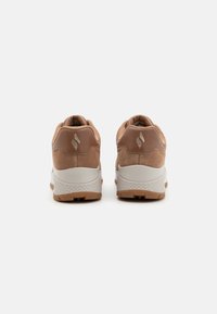 Brązowe zamszowe tenisówki z białą środkową podeszwą i teksturowaną gumową podeszwą zewnętrzną. Detal logo na pięcie, zaokrąglony kształt, wyściełany kołnierz dla wygody.