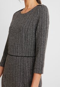 Strikkjole i sort og hvid, med et struktureret vævet mønster, rund halsudskæring og trekvartærmer samt en tætsiddende talje.