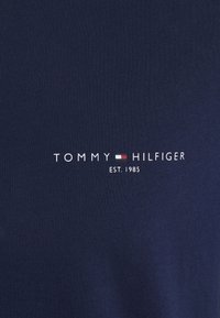 Tissu bleu marine avec le texte "Tommy Hilfiger" et un petit logo de drapeau rouge, blanc et bleu, "EST. 1985" imprimé sous le nom de la marque.