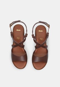 Brown leather sandals with a cross-strap design, cushioned footbed, and an adjustable buckle. Notable smooth texture and minimalistic styling.