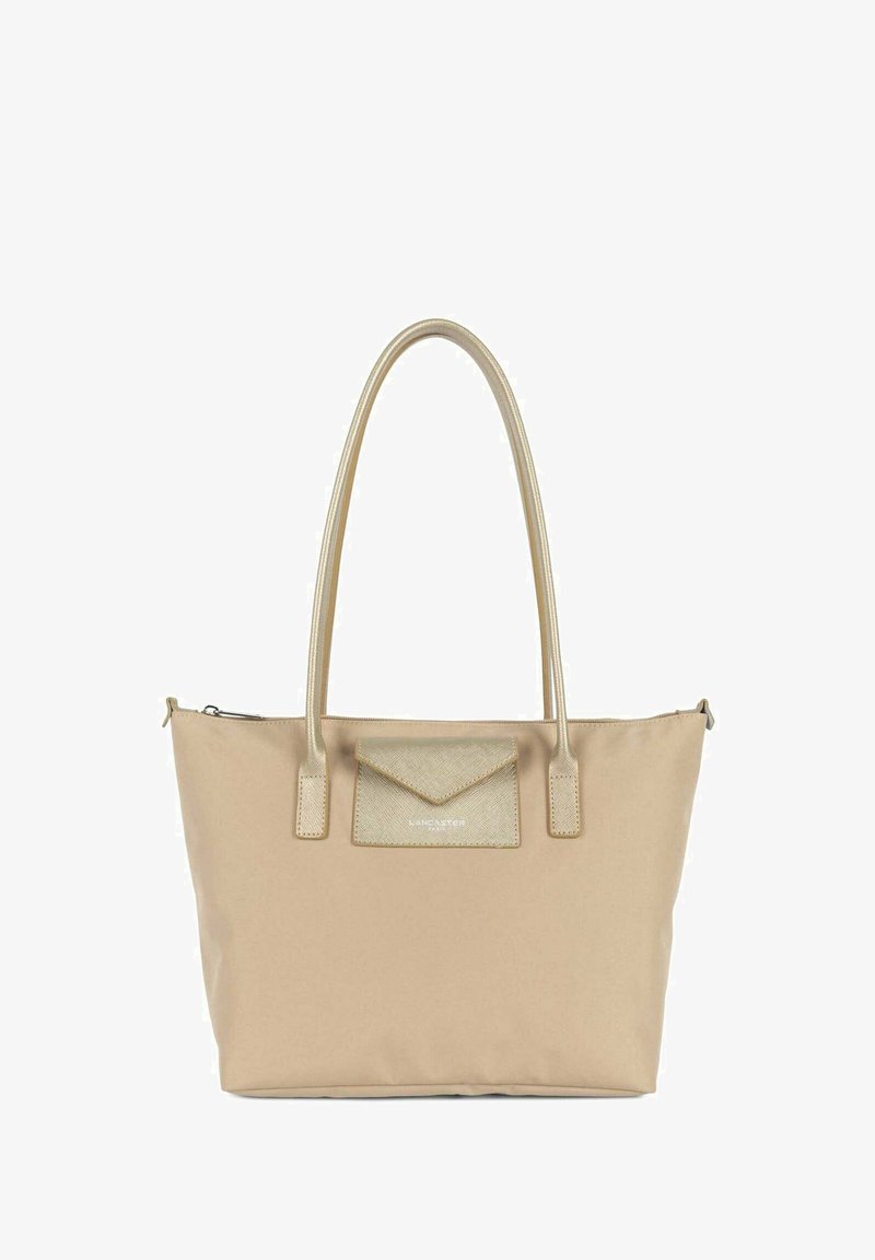 Beige tote bag med dobbelthåndtag, der har en tekstureret, metallisk accentlomme. Glat stof, lynlåslukning og subtile syninger.