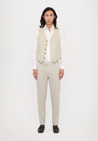 Beige Leinenweste mit fünf Knöpfen über einem weißen Hemd, kombiniert mit hellbeigen Hosen und dunklen Slippern. Schlichtes, maßgeschneidertes Design.
