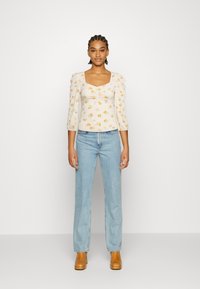 Blusa branca com estampado floral, mangas bufantes e decote quadrado, combinada com jeans azuis claros de perna reta e botas de salto castanhas.