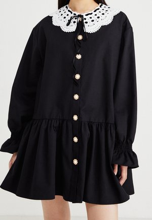 Black long-sleeve dress with ruffled hem, white scalloped lace collar, floral pearl buttons, and gathered cuffs on the sleeves.