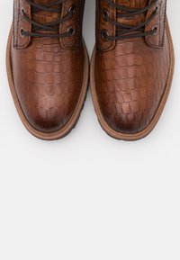 Chaussures en cuir marron avec un motif crocodile, bout rond, fermeture à lacets et semelle en caoutchouc texturée.