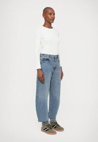 Valge pika varrukaga pluus, mugavad helesinised denim-püksid ning rohelised nokatsiga sneakers mustade triipudega. Pükstel on katkenud ääre detail.