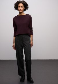 Tmavě fialový pletený svetr s širokým výstřihem, kombinovaný s upravenými černými kalhotami s texturou a černými kotníkovými botami. Hladké povrchové textury.