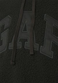 Sort fleece pullover med en struktureret overflade. Har et stort, hævet "GAP" logo i sort. Snoretræk i en matchende mørk farve.