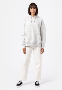 Gray hooded sweatshirt with a front pocket, loose fit, and adjustable drawstrings, paired with white pants and black sneakers.