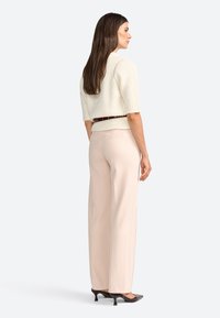 Maglione a maniche corte di colore crema, pantaloni palazzo in tonalità blush a vita alta e scarpe con tacco scuro. Una sottile cintura marrone mette in risalto la vita.