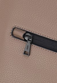 Cuero texturizado beige con un bolsillo con cremallera. Cremallera negra con una pestaña cuadrada que presenta el nombre de la marca "JOOP!" en letras pequeñas.
