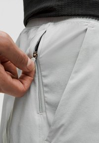 Šviesiai pilki sportiniai kelnių su užtraukiamu šoniniu kišeniu. Savybės - švelni, lygi tekstūra ir elastinga juosmens juosta patogumui.