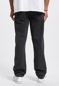 Pantalones de mezclilla negros con un corte relajado y puños elásticos, que cuentan con bolsillos traseros y una textura suave, combinados con zapatillas blancas.