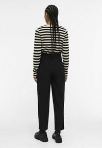 Chemise rayée à manches longues en noir et crème, associée à un pantalon noir taille haute. Présente des baskets noires à profil bas.